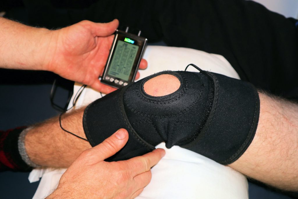 Image of a therapist looking at a knee with a therapeutic device to convey the importance of Sports Rehab Manhasset NY